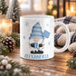 11 oz personalized winter gnome mug with blue snowflake hat, blue mug, snow shovel, blue snowflakes, and custom name printed below, displayed on a wooden table with cozy winter decor around it.