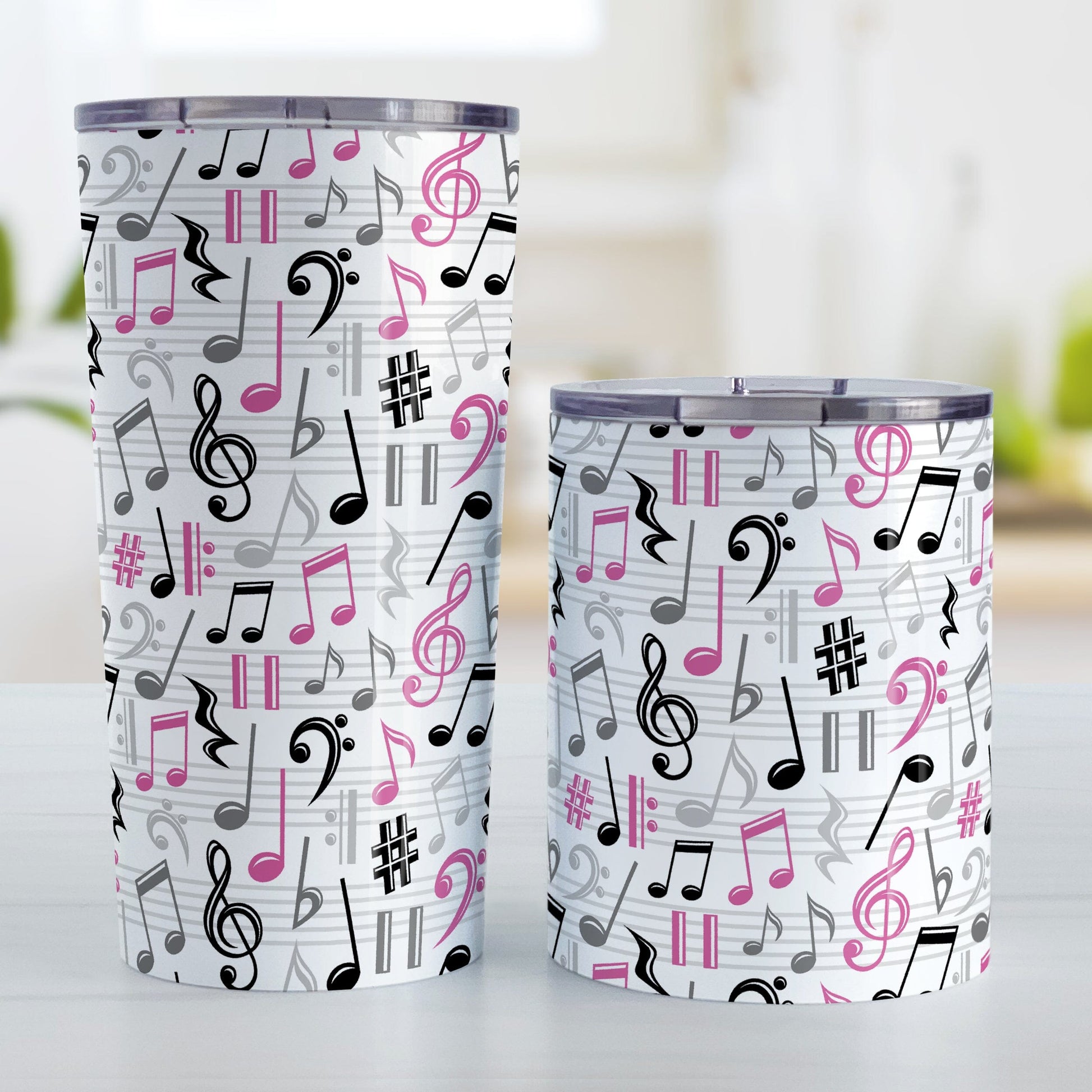 Pink Music Notes Pattern Tumbler Cups (20oz or 10oz) at Amy's Coffee Mugs. Stainless steel tumbler cups designed with music notes and symbols in pink, black, and gray in a pattern that wraps around the cups. Photo shows both sized cups on a table next to each other. 
