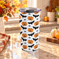 20 oz insulated stainless steel Halloween tumbler cup with orange jack-o'-lanterns, black bats, spiders, and light gray spider webs on white, on a granite countertop in a kitchen with fall decor including autumn plants, pumpkins, and an orange plaid tea towel.