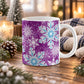 11 oz purple winter mug with large aqua blue and white snowflakes, dark purple snowflakes, and smaller accents across the pattern, shown on a wooden table with winter decor around it.