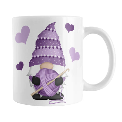 Purple Crochet Gnome Mug (11oz) at Amy's Coffee Mugs. A ceramic coffee mug designed with a cute gnome wearing a purple crochet hat while holding a ball of purple yarn and a crochet hook with purple hearts around him. This cute crochet gnome illustration is on both sides of the mug. 