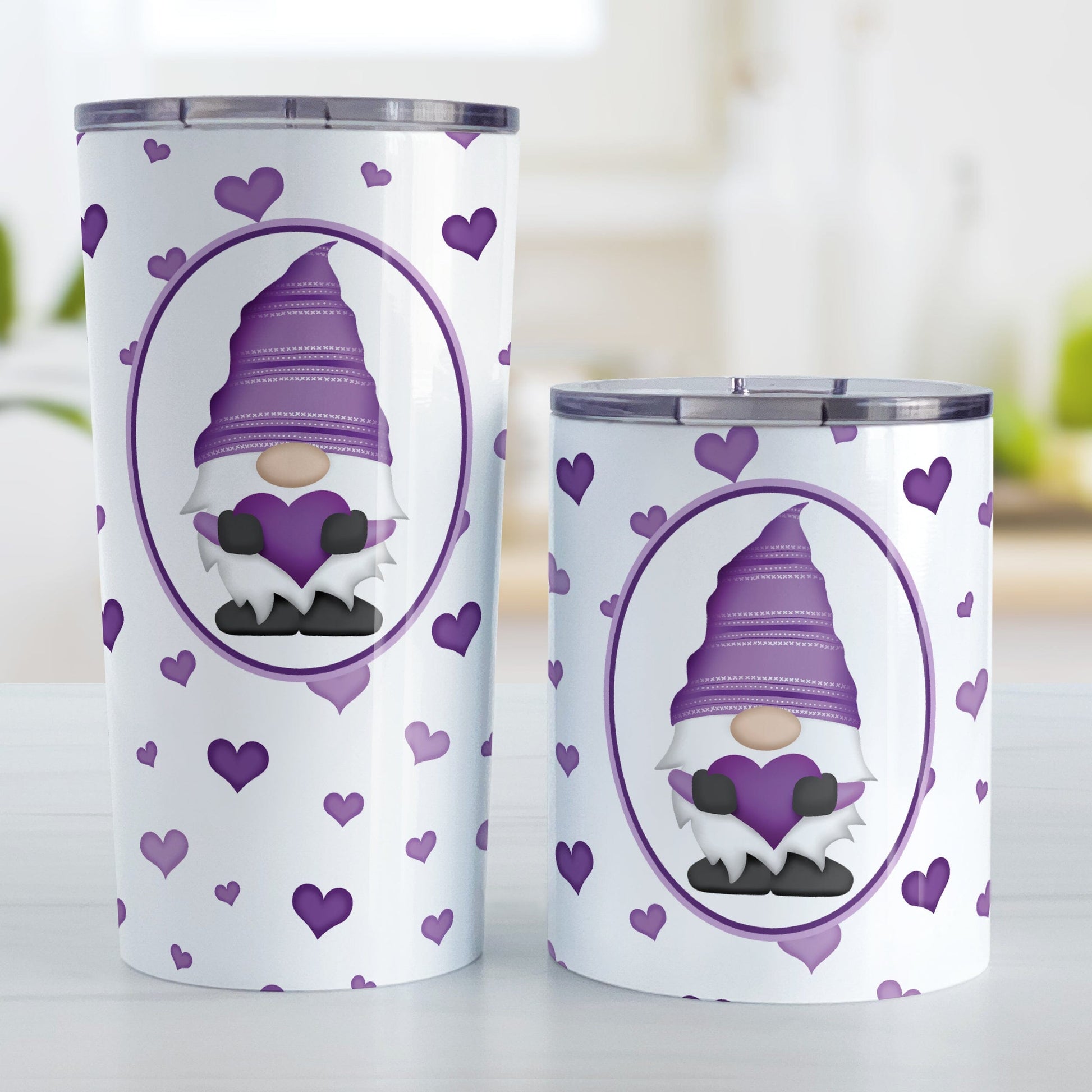 Purple Gnome Dainty Hearts Tumbler Cup (20oz or 10oz) at Amy's Coffee Mugs. Stainless steel tumbler cups designed with an adorable purple gnome holding a heart in a white oval over a pattern of cute and dainty hearts in different shades of purple that wrap around the cups. Photo shows both sized cups on a table next to each other. 