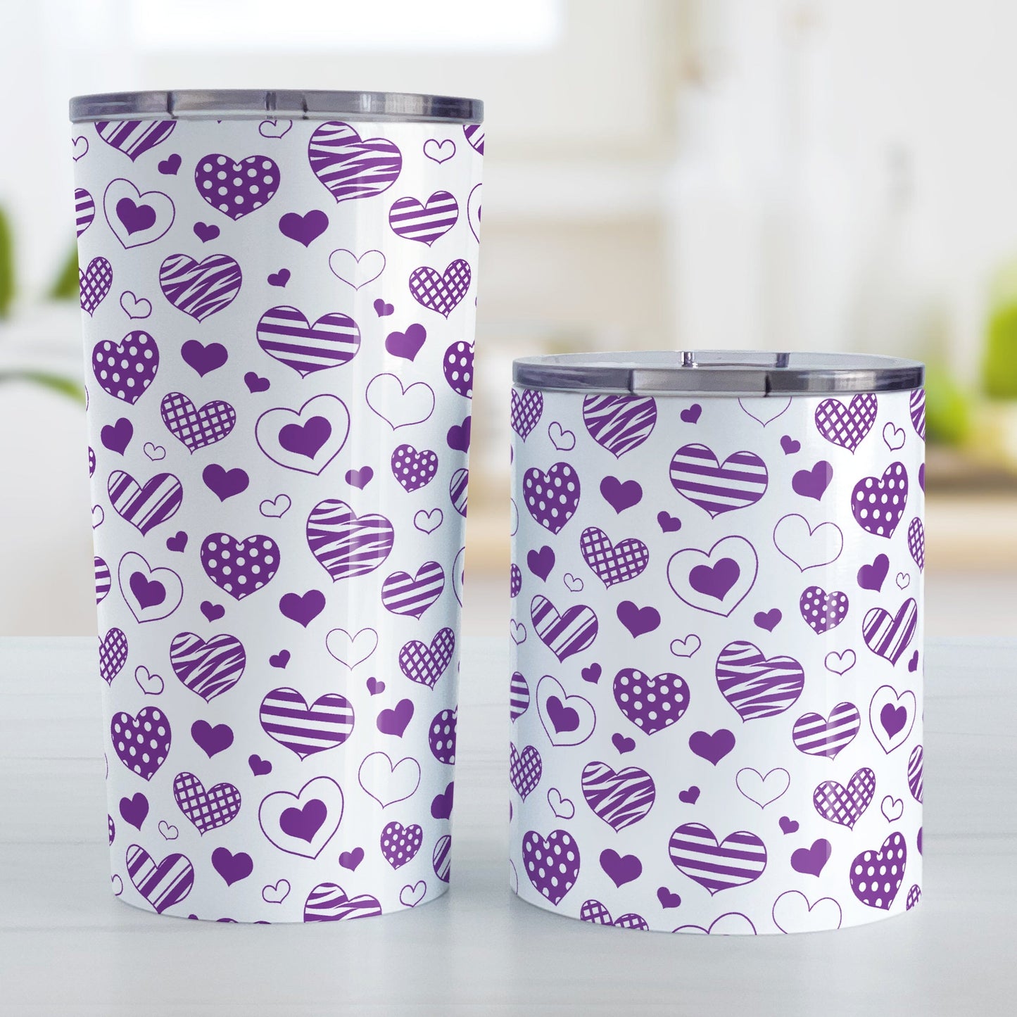 Purple Heart Doodles Tumbler Cup (20oz or 10oz) at Amy's Coffee Mugs. Stainless steel tumbler cups designed with a print of hand-drawn purple heart doodles in a pattern that wraps around the cups. This cute heart pattern is perfect for Valentine's Day or for anyone who loves hearts and young-at-heart drawings. Photo shows both sized cups on a table next to each other.