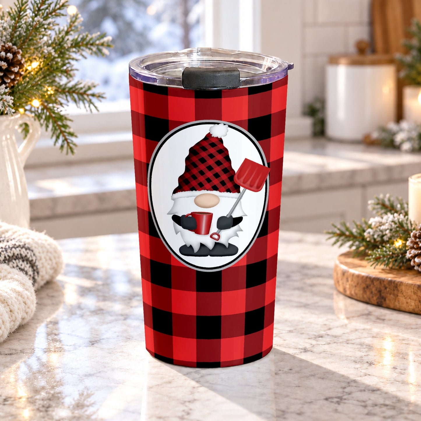 20 oz red gnome buffalo plaid tumbler cup with winter gnome holding a red mug and snow shovel on a red and black buffalo check background, on a granite countertop in a kitchen with light rustic winter decor including pine cones, pine boughs, and a cozy blanket.