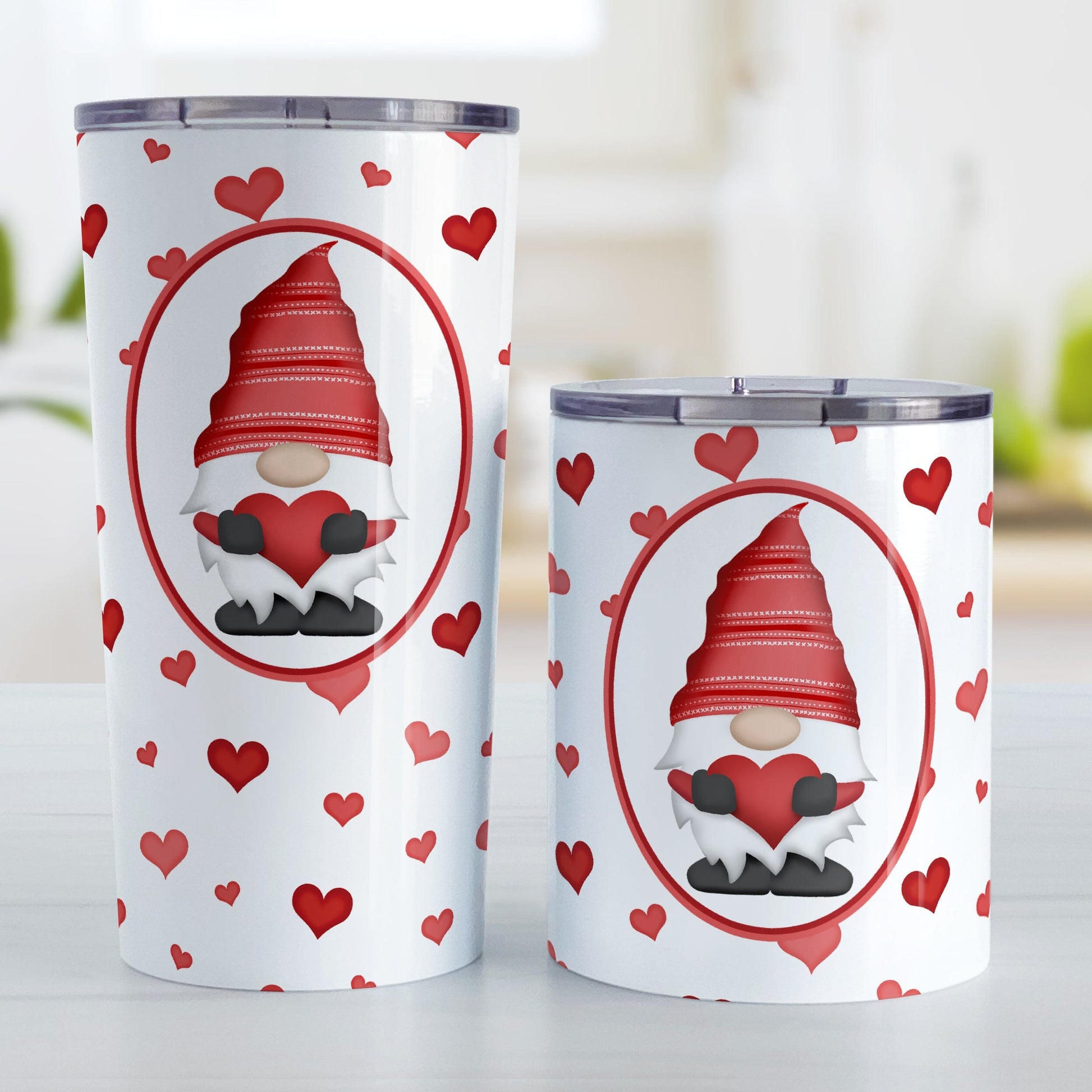 Red Gnome Dainty Hearts Tumbler Cup (20oz or 10oz) at Amy's Coffee Mugs. Stainless steel tumbler cups designed with an adorable red gnome holding a heart in a white oval over a pattern of cute and dainty hearts in different shades of red that wrap around the cups. Photo shows both sized cups on a table next to each other. 