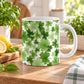 A white ceramic mug decorated with a green shamrock and clover pattern, sitting on a wooden table in a bright kitchen setting with lemons and plants for spring.