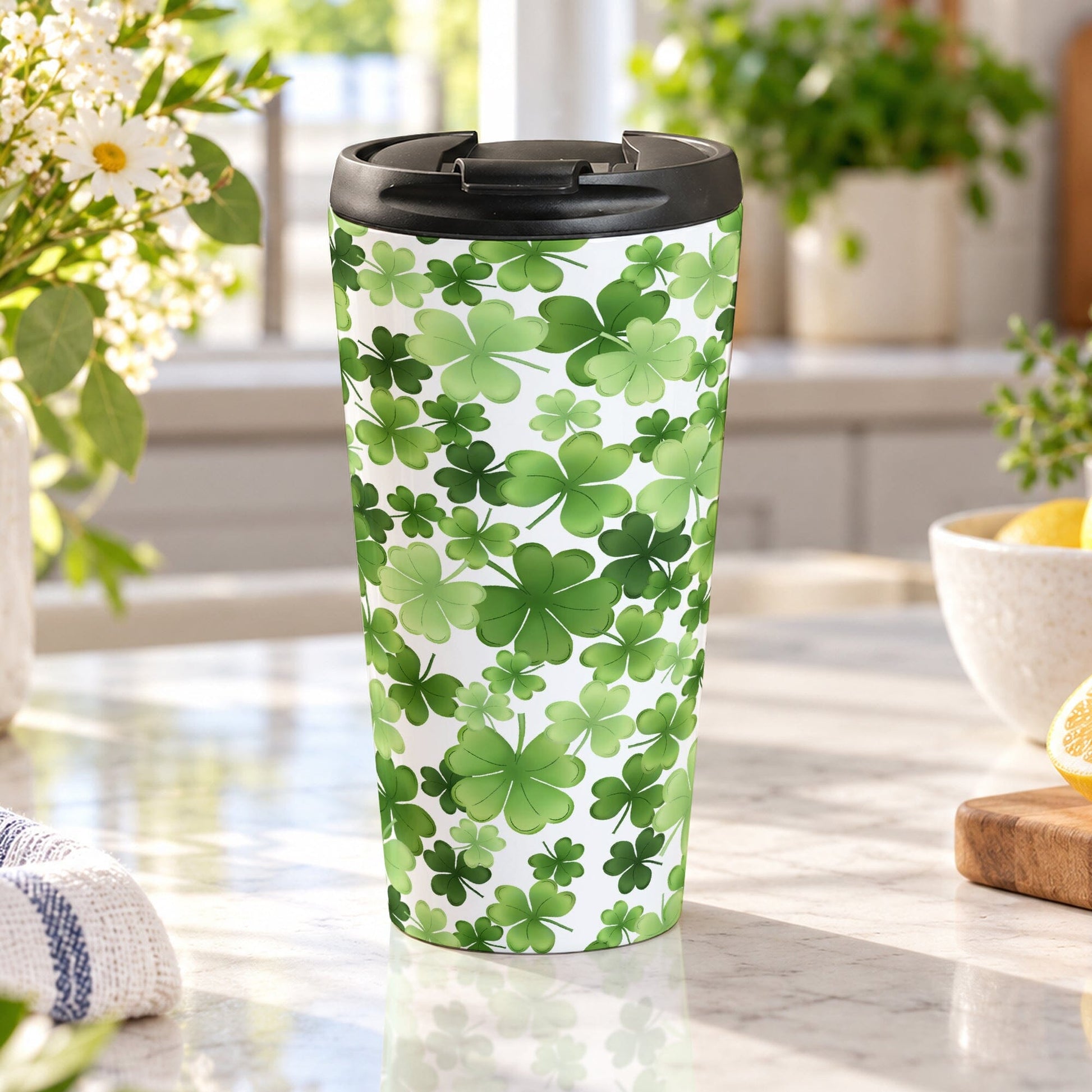 15 oz Shamrocks and 4-Leaf Clovers Travel Mug with green shamrocks and four-leaf clovers in varied shades and sizes, in a kitchen on a granite countertop with green plants, daisies, lemons, and a tea towel around it.