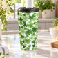 15 oz Shamrocks and 4-Leaf Clovers Travel Mug with green shamrocks and four-leaf clovers in varied shades and sizes, in a kitchen on a granite countertop with green plants, daisies, lemons, and a tea towel around it.