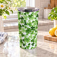 20 oz insulated stainless steel tumbler cup covered with green shamrocks and four-leaf clovers in multiple shades on a white background, on a granite countertop in a bright kitchen with green plants, daisies, a plaid tea towel, and lemons on a wood cutting board.