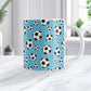 11oz white ceramic coffee mug with a pattern of soccer balls on a blue background, sitting on a white marble countertop