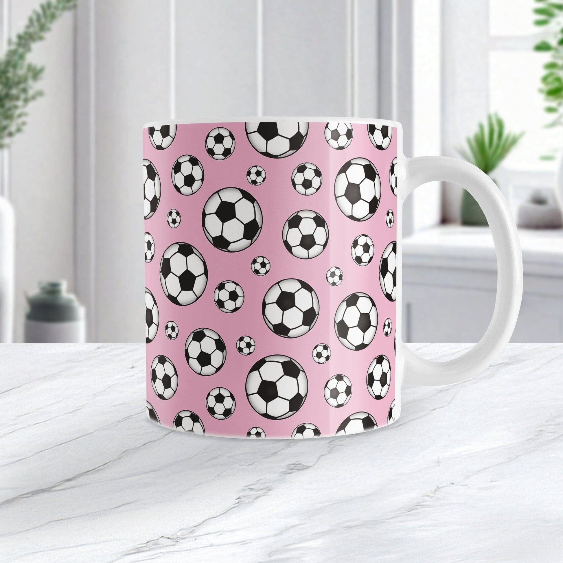 11oz white ceramic mug with a design of soccer balls over pink, on a marble countertop