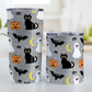 Spooky Cute Halloween Tumbler Cup (20oz or 10oz) at Amy's Coffee Mugs. A tumbler cup designed with a cute black cat, ghost, jack o'lantern, crescent moon, bat, spider, and spider webs over a gray background color in a pattern that wraps around the cup. Photo shows both sized cups on a table next to each other.