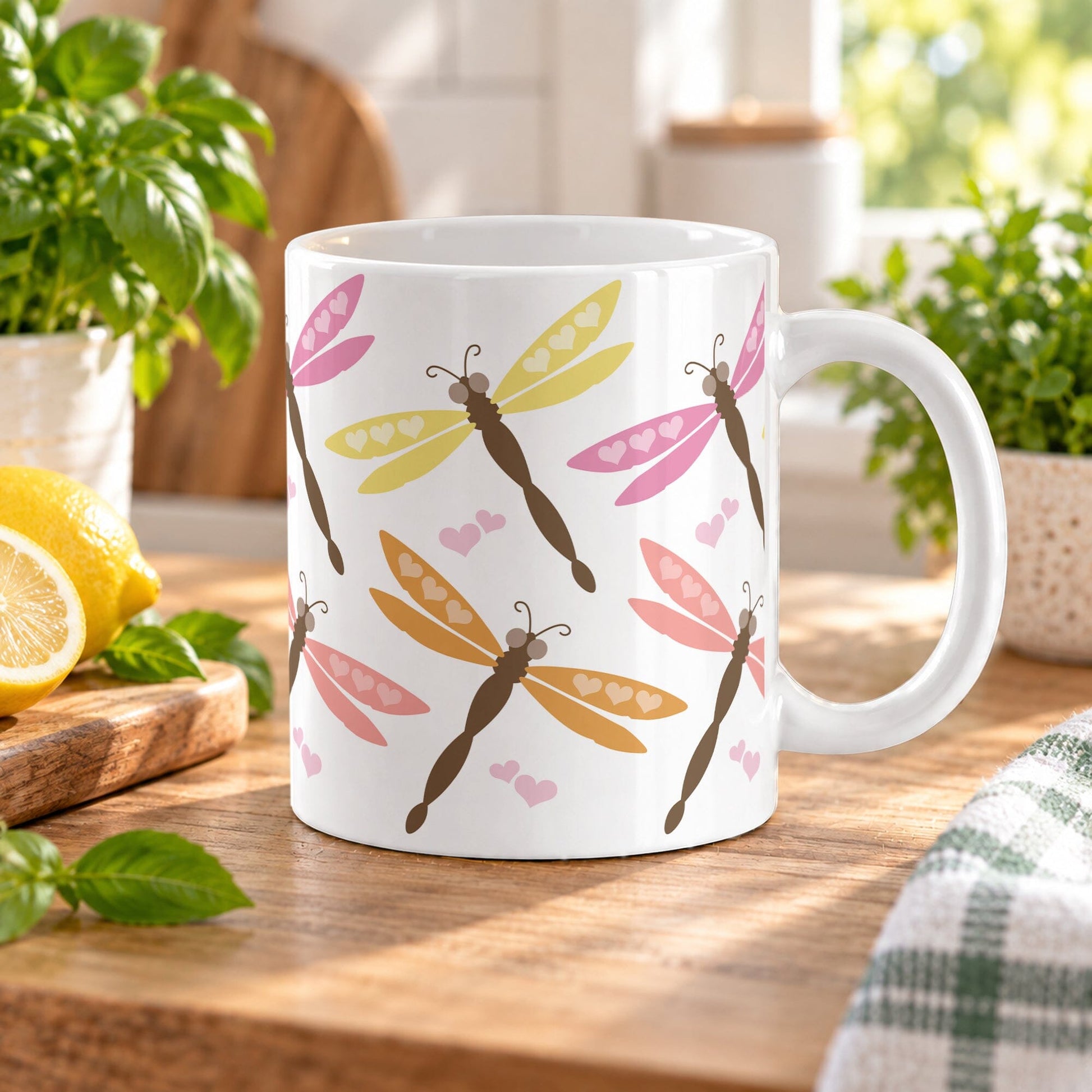 11 oz Summer Dragonfly Mug with pink, peach, orange, yellow, and brown dragonflies with heart accents, set on a wooden table in a bright kitchen environment with basil, lemon, and plants in the background.