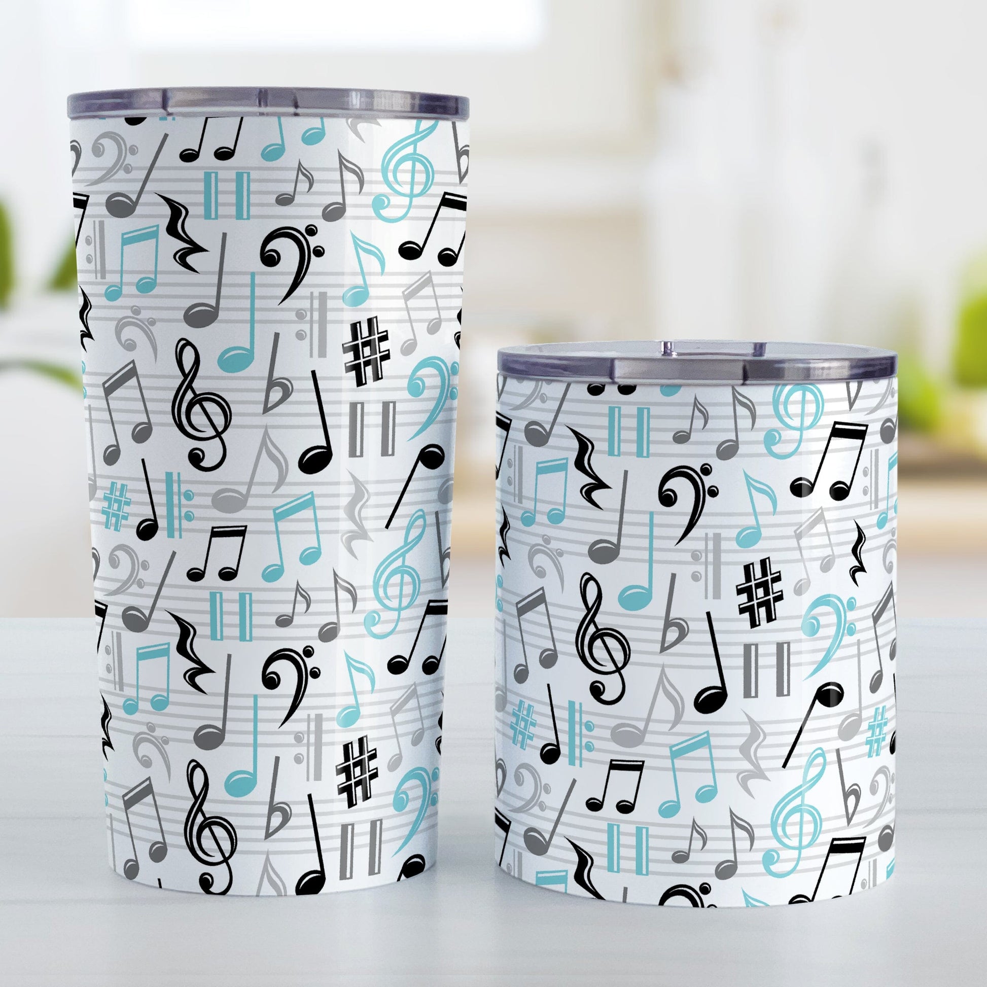 Turquoise Music Notes Pattern Tumbler Cups (20oz or 10oz) at Amy's Coffee Mugs. Stainless steel tumbler cups designed with music notes and symbols in turquoise, black, and gray in a pattern that wraps around the cups. Photo shows both sized cups on a table next to each other.