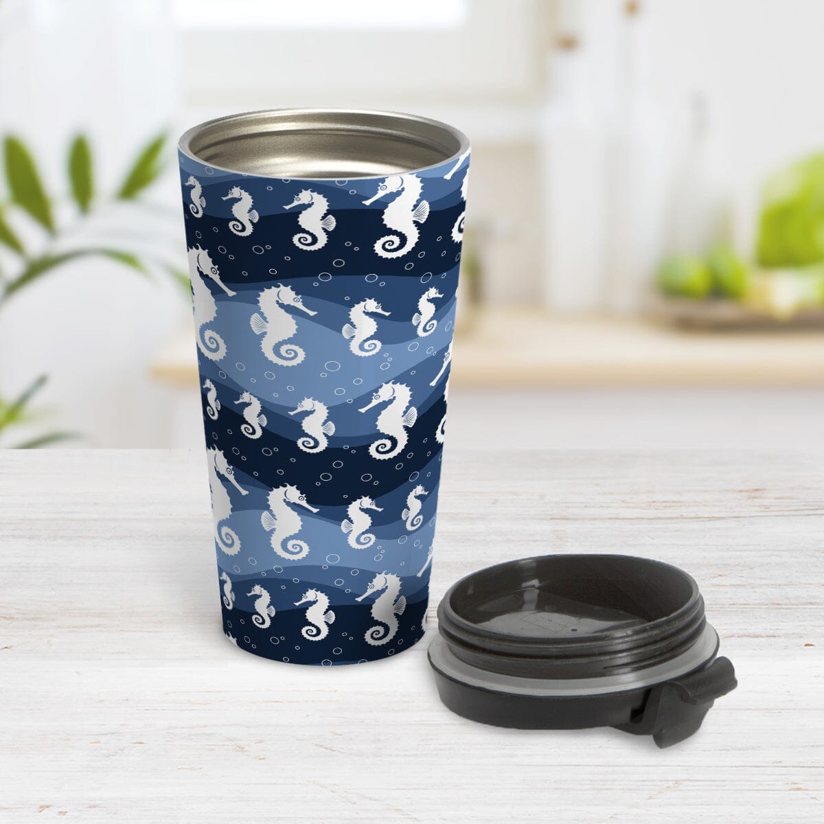 Wavy Blue Seahorse Travel Mug at Amy's Coffee Mugs. A 15oz travel mug designed with white silhouette seahorses over a wavy blue background in different shades of navy blue with white circle line bubbles all in a pattern that wraps around the travel mug. Photo shows the mug open on a table with its lid beside it.