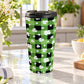 15 oz green and black buffalo plaid travel mug with white shamrocks and four-leaf clovers, displayed in a bright kitchen on a granite countertop with green plants, daisies, a teal towel, and lemons in a bowl and on a cutting board.