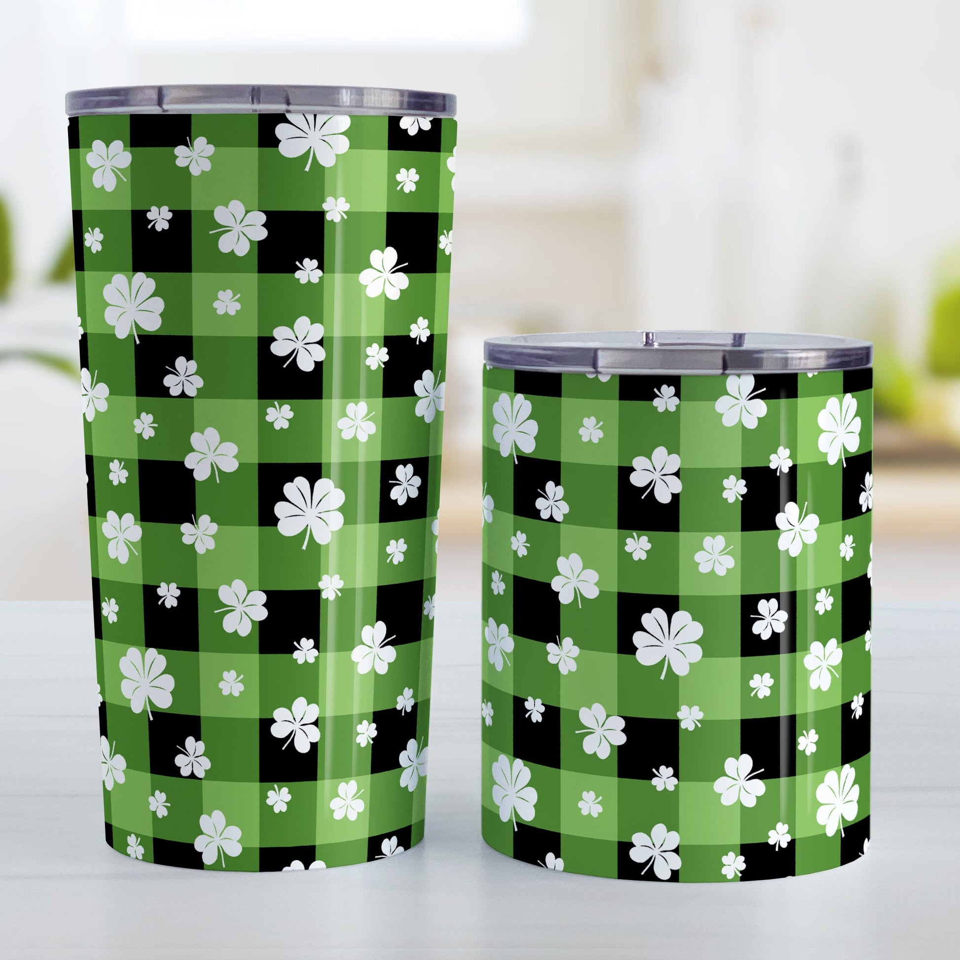 20oz and 10oz tumbler cups with green and black checkered (buffalo plaid) pattern and white clovers. Photo shows both sized cups on a table next to each other.