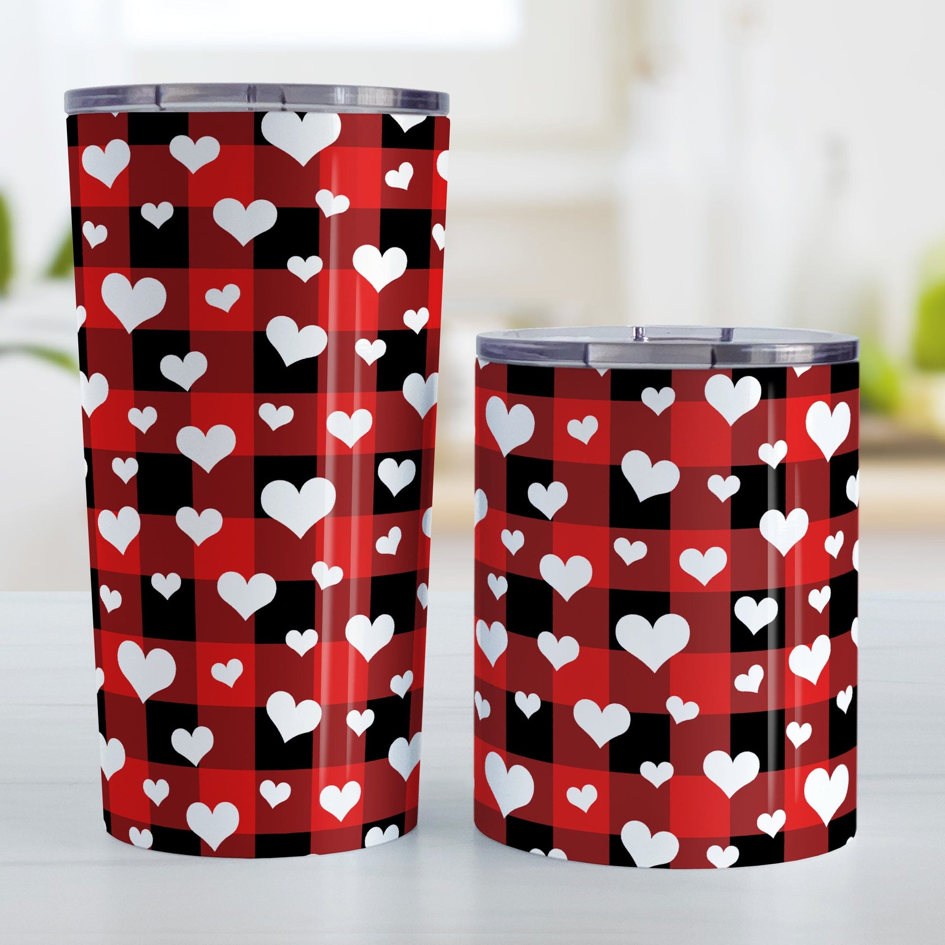 20oz and 10oz tumbler cups with a red and black buffalo plaid pattern and white hearts. Photo shows both sized cups on a table next to each other