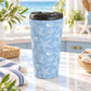 15 oz blue beach travel mug with white line-art seashells, starfish, and coastal shell illustrations, displayed on a granite countertop in a beach house kitchen with coastal decor.