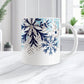 Winter Blue Silver Snowflake Mug (11oz) at Amy's Coffee Mugs. A ceramic coffee mug with navy blue, aqua blue, and silver-colored glitter-illustrated snowflakes along the top, cascading down most of the mug, over white. This wintry snowflake design wraps around the mug up to the handle. Image shows the mug on a white marble countertop.