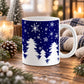 11 oz winter snow mug with white pine trees, falling snow, and assorted snowflakes against a navy blue background, on a wooden table with winter decor around it.