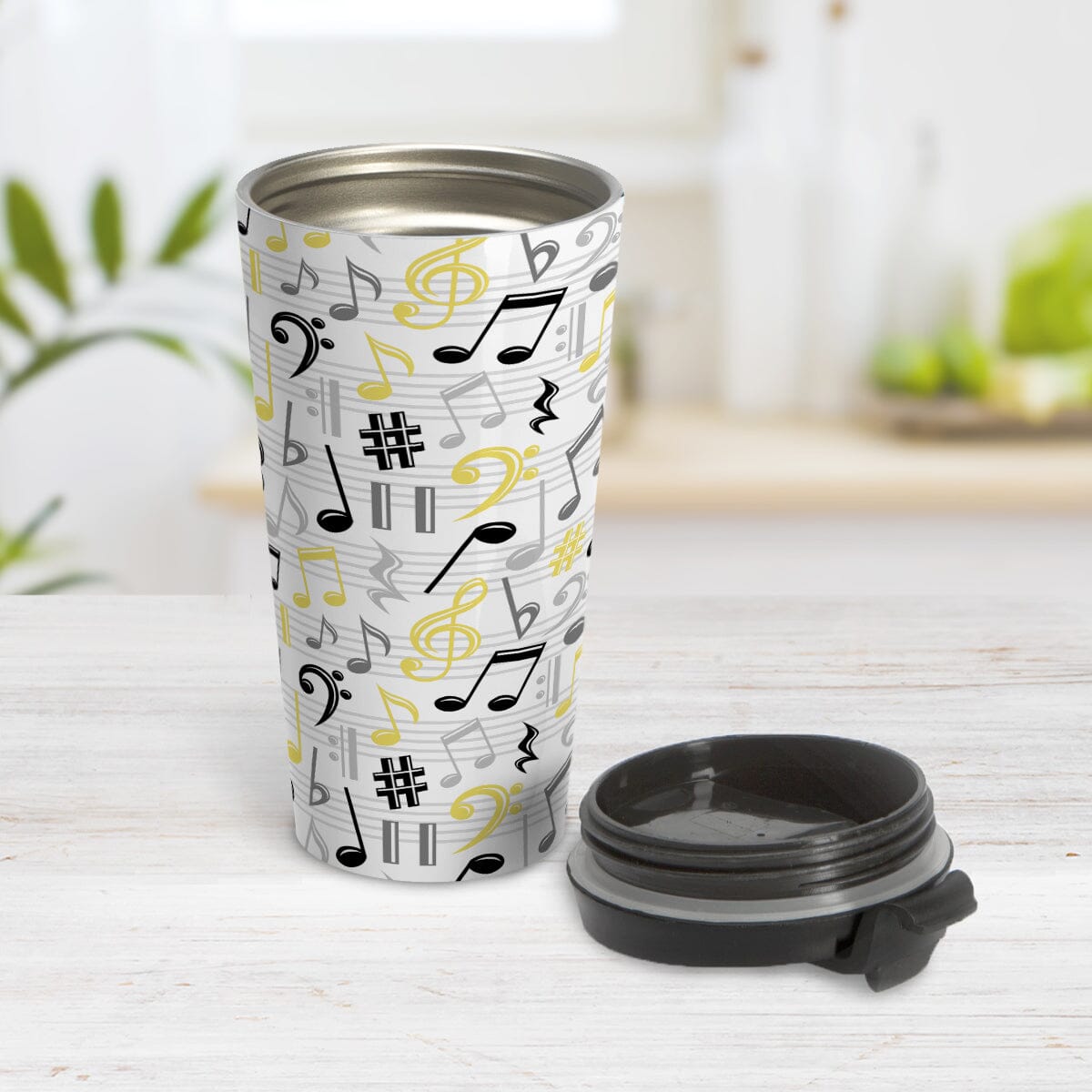 Yellow Music Notes Pattern Travel Mug (15oz) at Amy's Coffee Mugs. A stainless steel travel mug designed with music notes and symbols in yellow, black, and gray in a pattern that wraps around the travel mug. Image shows the travel mug open with the lid laying beside it on a tabletop.