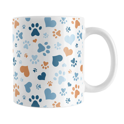 Blue Hearts and Paw Prints Mug (11oz) at Amy's Coffee Mugs. A ceramic coffee mug designed with a pattern of hearts and paw prints in orange and different shades of blue that wraps around the mug to the handle. This mug is perfect for people love dogs and cute paw print designs.