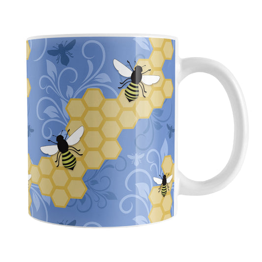 Blue Honeycomb Bee Mug (11oz) at Amy's Coffee Mugs. A ceramic coffee mug designed with a pattern of black and yellow bees on honeycomb lines over a blue flourish background that wraps around the mug to the handle.