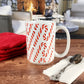 Candy Cane Pattern Mug (15oz) on a walnut table with a spoon and red towel with a cabin background.