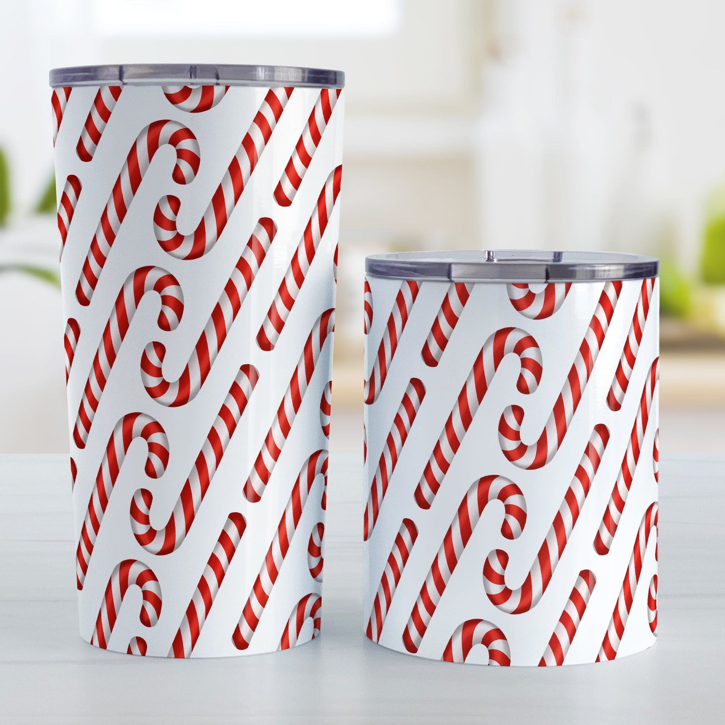 Candy Cane Pattern Tumbler Cup (20oz or 10oz) at Amy's Coffee Mugs. Stainless steel tumbler cups designed with a diagonal pattern of red and white striped candy canes that wraps around the cups. Photo shows both sized cups on a table next to each other.