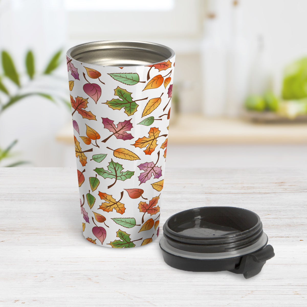 Changing Leaves Fall Travel Mug (15oz) at Amy's Coffee Mugs. A stainless steel insulated travel mug designed with a fall themed pattern of leaves changing colors, as they do at the beginning of autumn, that wraps around the travel mug. Photo shows the mug open with the lid on the table beside it.