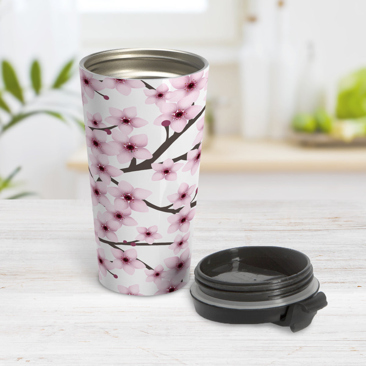 Cherry Blossom Travel Mug (15oz) at Amy's Coffee Mugs. A stainless steel insulated travel mug designed with a pattern of pink cherry blossom flowers on branches that wraps around the travel mug. Photo shows the travel mug open with the lid on the table beside it.