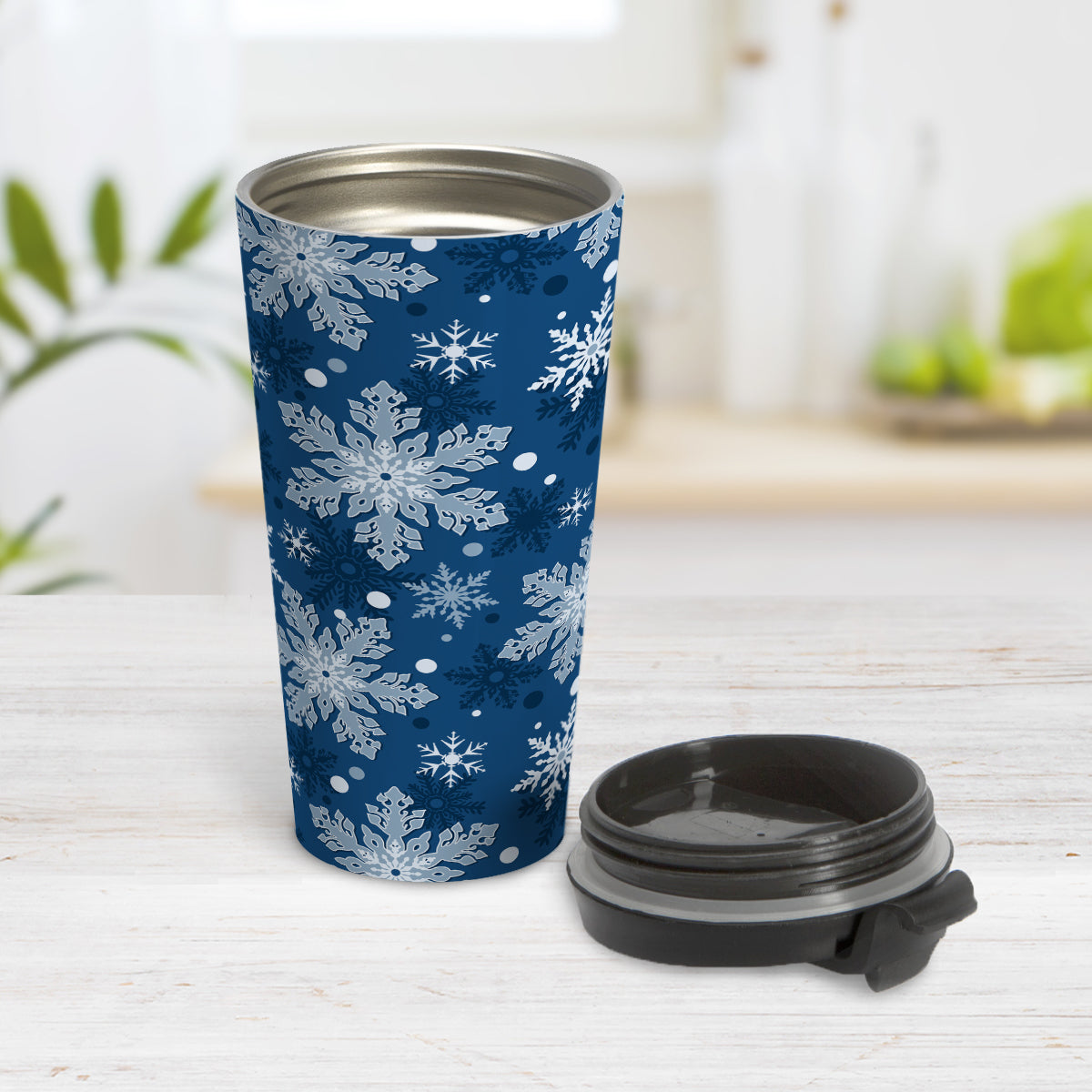 Classic Blue Snowflake Pattern Winter Travel Mug (15oz) at Amy's Coffee Mugs. A stainless steel insulated travel mug designed with a pattern of different shades of blue snowflakes over a classic blue background color that wraps around the travel mug. Photo shows the mug open with the lid on the table beside it.
