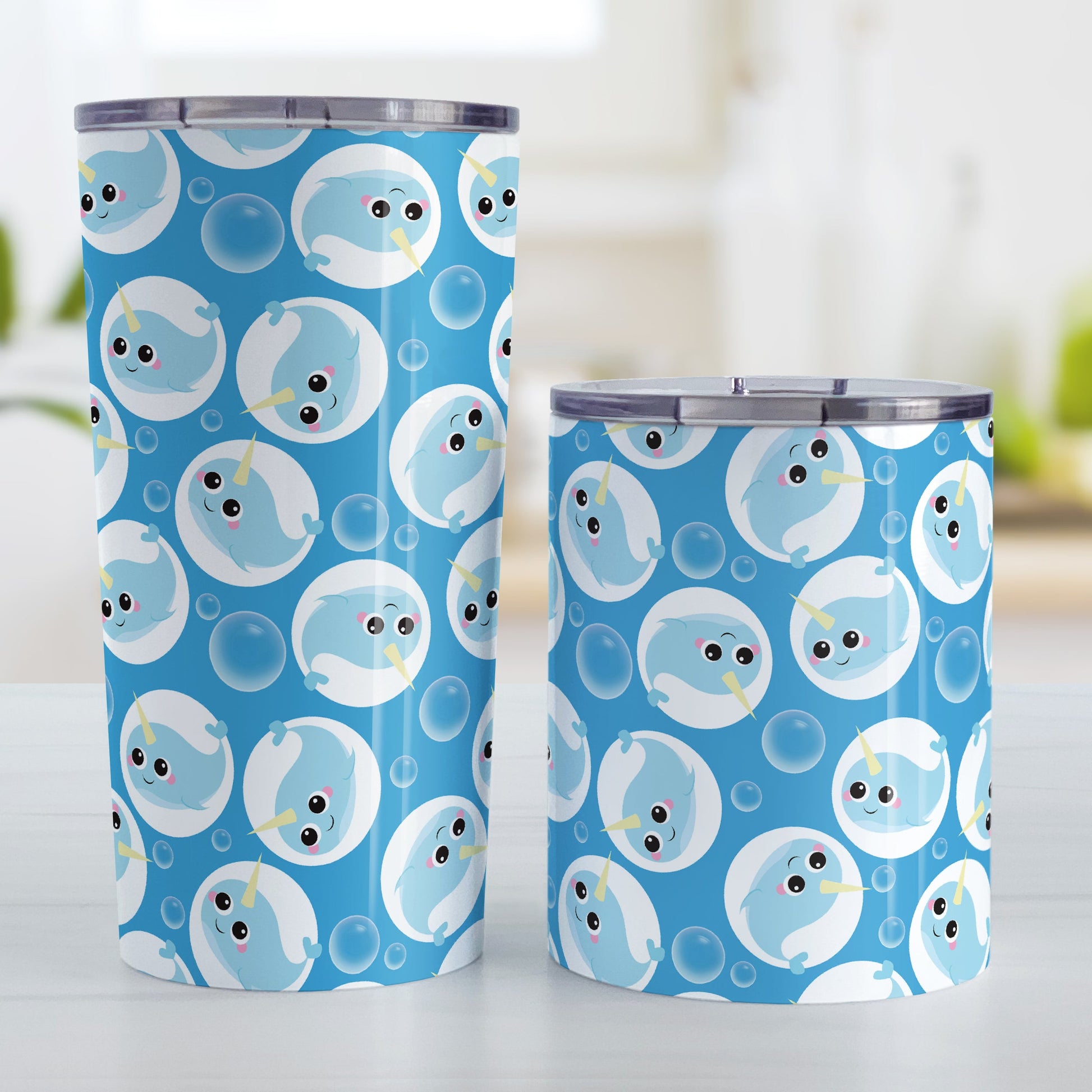 Cute Blue Narwhal Bubble Pattern Tumbler Cup (20oz and 10oz, stainless steel insulated) at Amy's Coffee Mugs. A tumbler cup designed with cute light blue narwhals in white circles and with bubbles scattered over a blue background color in a pattern that wraps around the cup. Photo shows both sized cups on a table next to each other.