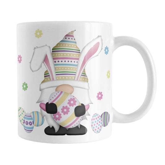 Easter Eggs Bunny Gnome Mug (11oz) at Amy's Coffee Mugs. A ceramic coffee mug designed with an adorable gnome with bunny ears and holding a large Easter egg. Colorful little Easter eggs lay on the ground beside him with little flowers floating around.