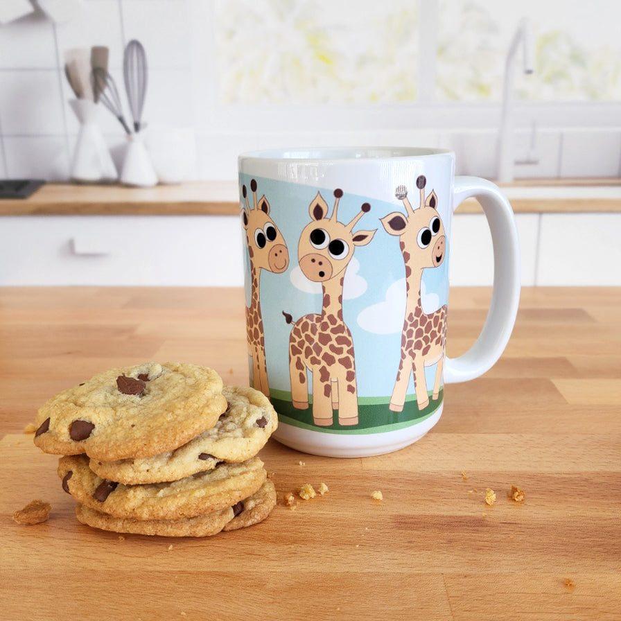 Gathering Giraffes Mug (15oz) at Amy's Coffee Mugs. A ceramic coffee mug designed with five cute illustrated giraffes, with different expressions, around the mug, over a blue sky and green grass background. Photo shows the mug on a kitchen island next to cookies. 