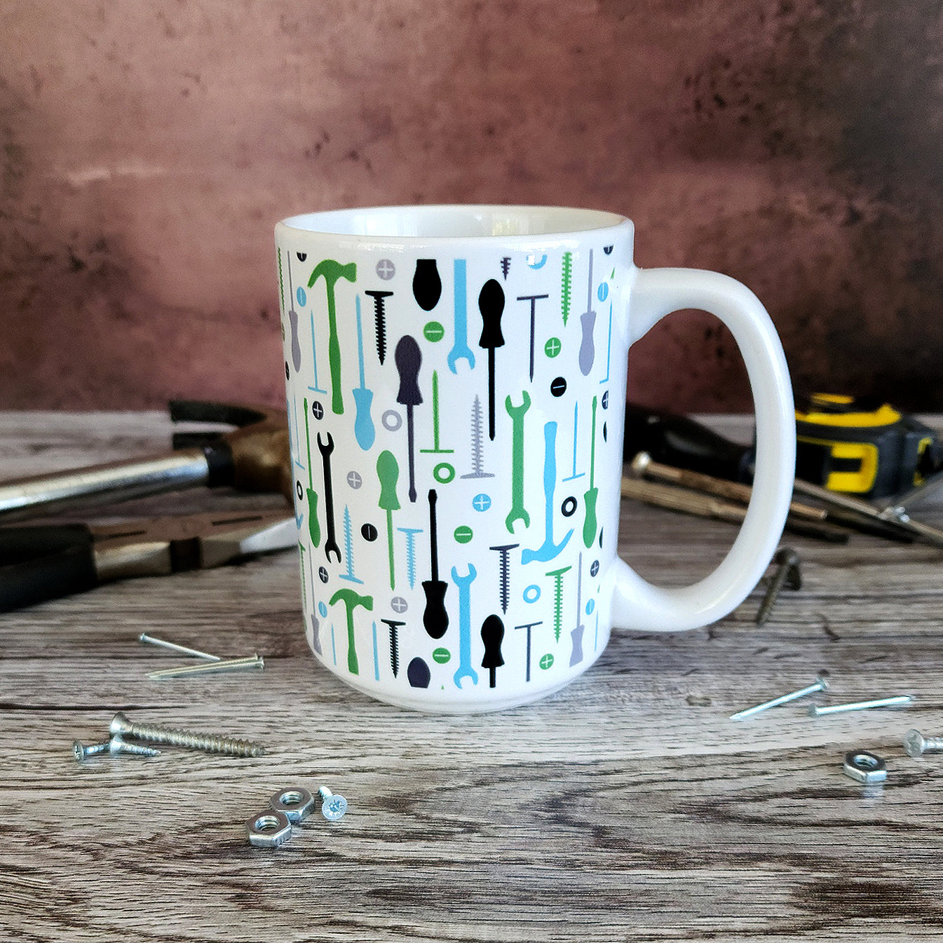 Green Blue Tools Pattern Mug (15oz on work bench with tools round it) at Amy's Coffee Mugs. A ceramic coffee mug with a modern style pattern of tools in green, blue, black, and gray over white that wraps around the mug to the handle. Perfect for any handyman or contractor. 