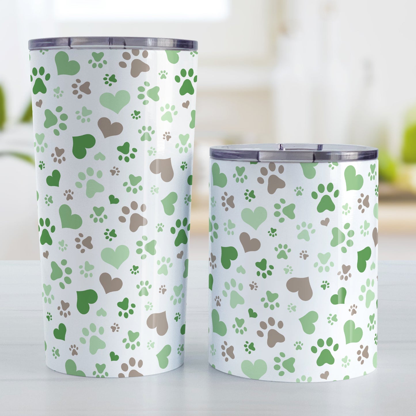 Green Hearts and Paw Prints Tumbler Cup (20oz and 10oz) at Amy's Coffee Mugs. Stainless steel insulated tumbler cups designed with a pattern of hearts and paw prints in brown and different shades of green that wraps around the cups. These tumbler cups are perfect for people love dogs and cute paw print designs. The photo shows both sized cups next to each other. 