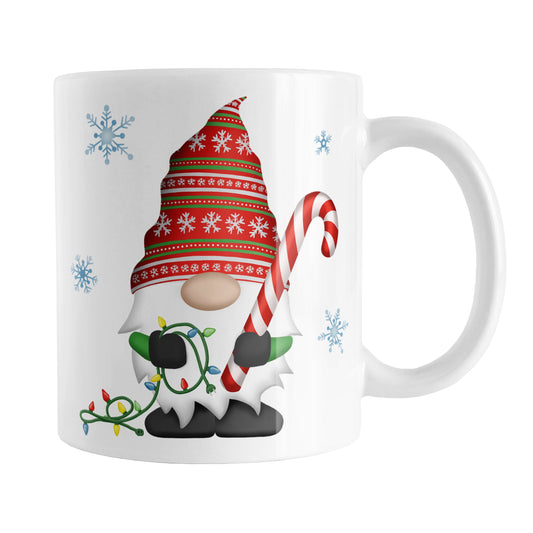 Holiday Candy Cane Gnome Mug (11oz) at Amy's Coffee Mugs. A ceramic coffee mug designed with a holiday gnome on both sides of the mug wearing a festive red and green snowflake hat and holding a large candy cane and a string of Christmas lights, with winter snowflakes around it.