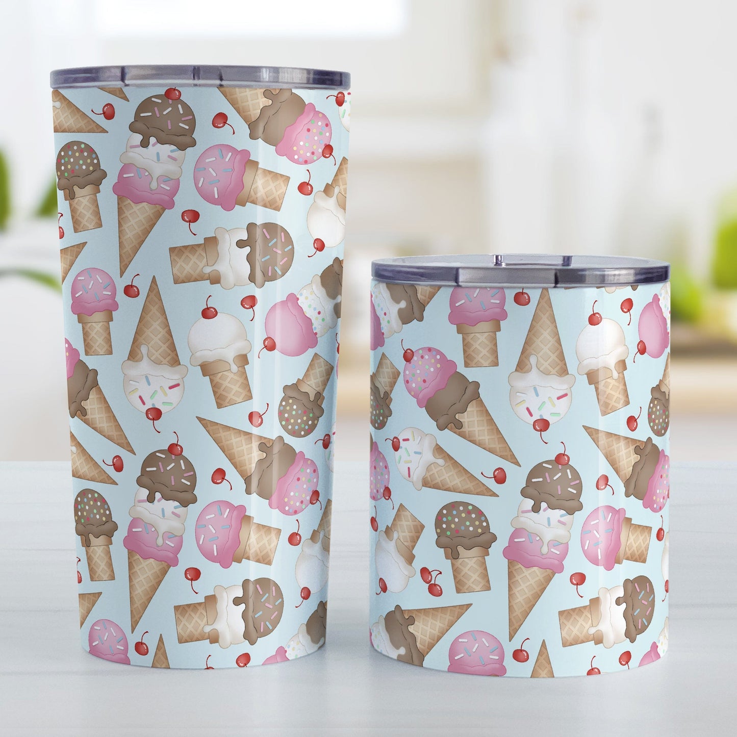 Ice Cream Cones Pattern Tumbler Cup (20oz or 10oz) at Amy's Coffee Mugs. Stainless steel tumbler cups printed with a design of hand-drawn ice cream cones with chocolate, strawberry, and vanilla scoops, with sprinkles and cherries, over a pale blue color, in a pattern that wraps around the cups. Photo shows both size cups on a table next to each other.