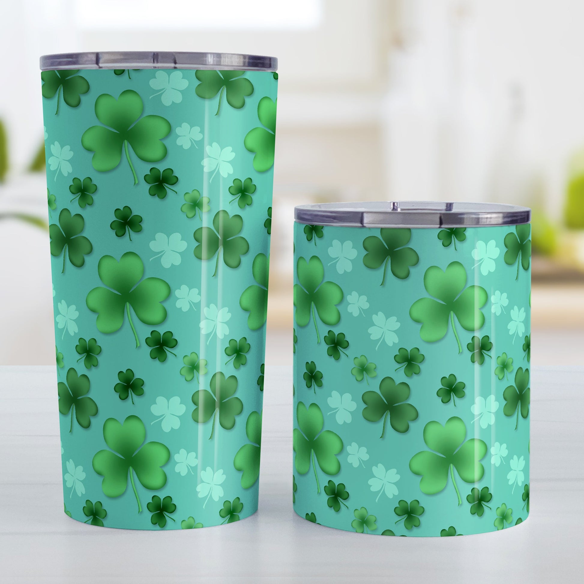 Lucky Clover Pattern Teal and Green Tumbler Cup (20oz and 10oz, stainless steel insulated) at Amy's Coffee Mugs. Tumbler cups designed with a lucky green clover pattern with a 4-leaf clover among 3-leaf clovers, in different shades of green, over a teal background that wraps around the cups. Photo shows both sized cups next to each other.