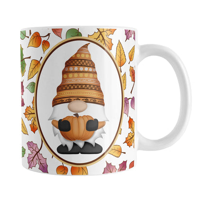 Orange Gnome Fall Leaves Mug (11oz) at Amy's Coffee Mugs. A ceramic coffee mug designed with an adorable orange hat gnome holding an orange pumpkin in a white oval over a pattern of leaves in different fall colors that wrap around the mug to the handle.