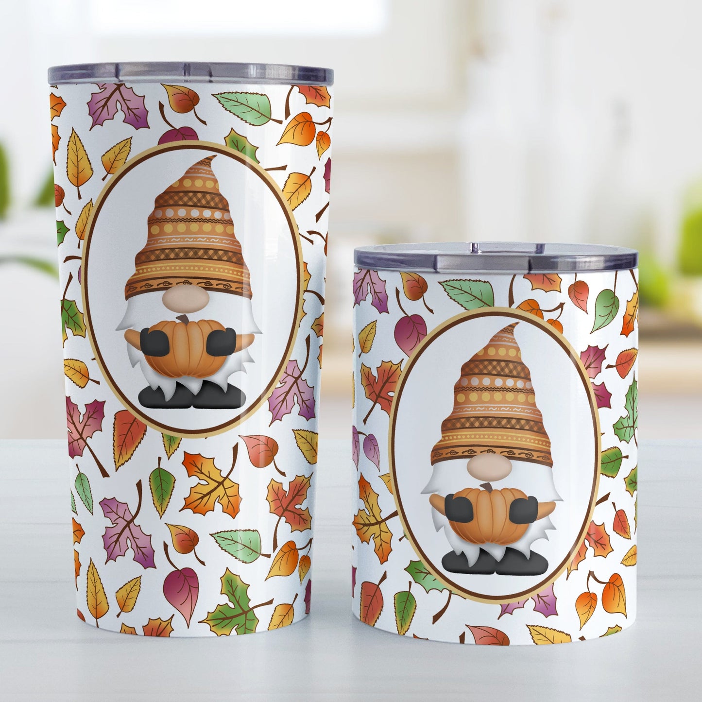 Orange Gnome Fall Leaves Tumbler Cup (20oz or 10oz) at Amy's Coffee Mugs. Stainless steel tumbler cups designed with an adorable orange hat gnome holding an orange pumpkin in a white oval over a pattern of leaves in different fall colors that wrap around the cups. Photo shows both sized cups next to each other on a table.