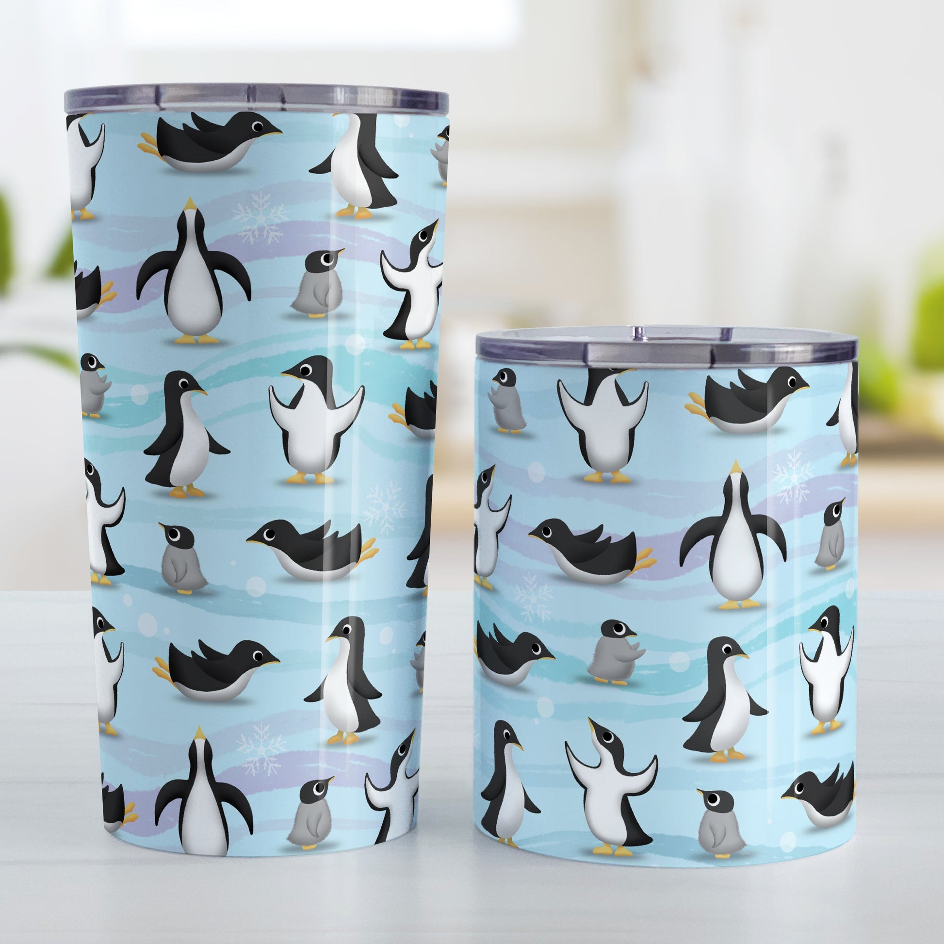 Penguin Parade Pattern Tumbler Cup (20oz and 10oz, stainless steel insulated) at Amy's Coffee Mugs. Tumbler cups designed with a fun penguin parade pattern featuring a variety of penguins and baby penguins over an Antarctic background with waves of blue, turquoise, and purple colors with hints of snowflakes that wraps around the cups. Photo shows both sized cups next to each other.