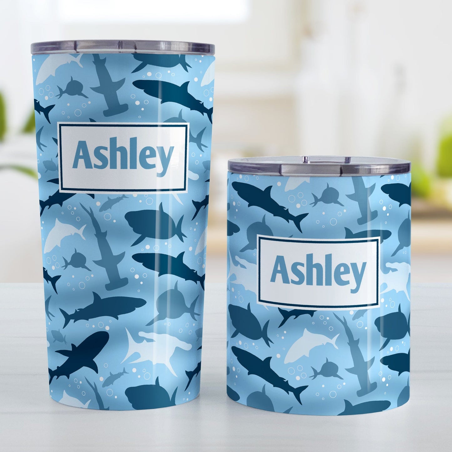 Personalized Blue Frenzy Sharks Tumbler Cups (20oz or 10oz) at Amy's Coffee Mugs. Stainless steel insulated tumbler cups designed with a pattern of sharks in different shades of blue, in a frenzy deep beneath the water, that wraps around the cups. Your personalized name is custom printed in blue over the shark pattern. Photo shows both sized cups next to each other. 