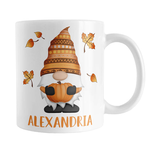 Personalized Fall Pumpkin Gnome Mug (11oz) at Amy's Coffee Mugs. A ceramic coffee mug designed with a fall themed gnome holding an orange pumpkin with an orange festive hat, and leaves in the air around it, on both sides of the mug. Your personalized name is custom printed in orange below the gnome. 