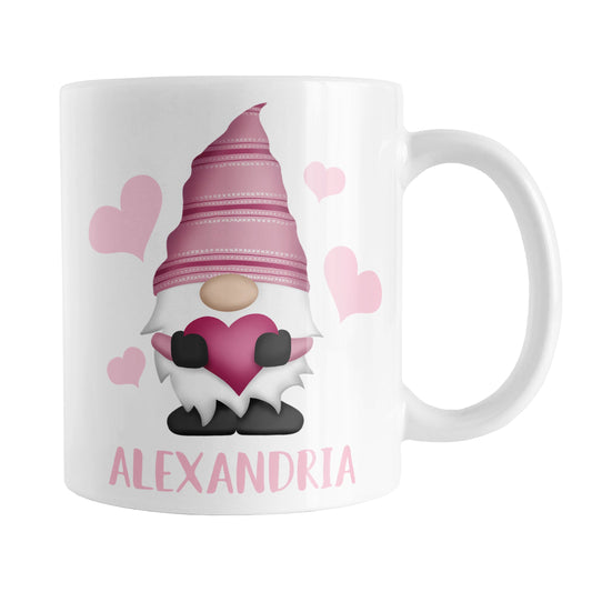 Personalized Pink Heart Gnome Mug (11oz) at Amy's Coffee Mugs. A ceramic coffee mug designed with an illustration of an adorable gnome with a pink pointed hat, holding a big pink heart, with light pink hearts around it. Below the gnome is your personalized name custom printed in a cute pink font. This charming gnome and personalized name are printed on both sides of the mug.