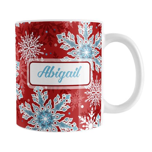 Personalized Red Blue Snowflake Winter Mug (11oz) at Amy's Coffee Mugs. A ceramic coffee mug designed with a pattern of aqua blue and white snowflakes over a red background color that wraps around the mug to the handle. Your name is custom printed in an aqua blue script font on both sides of the mug.