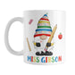Personalized School Teacher Gnome Mug (11oz) at Amy's Coffee Mugs. A ceramic coffee mug designed with an illustration of an adorable gnome wearing a festive hat with numbers and letters in primary colors and holding a large oversized pencil and graded A+ paper. Around the gnome are an eraser, a ruler, and a red apple. Your personalized name or your teacher's name is custom printed below the gnome in blue, red, yellow, and green alternating colored letters.
