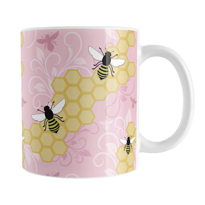 Pink Honeycomb Bee Mug (11oz) at Amy's Coffee Mugs. A ceramic coffee mug designed with a pattern of black and yellow bees on honeycomb lines over a pink flourish background that wraps around the mug to the handle.